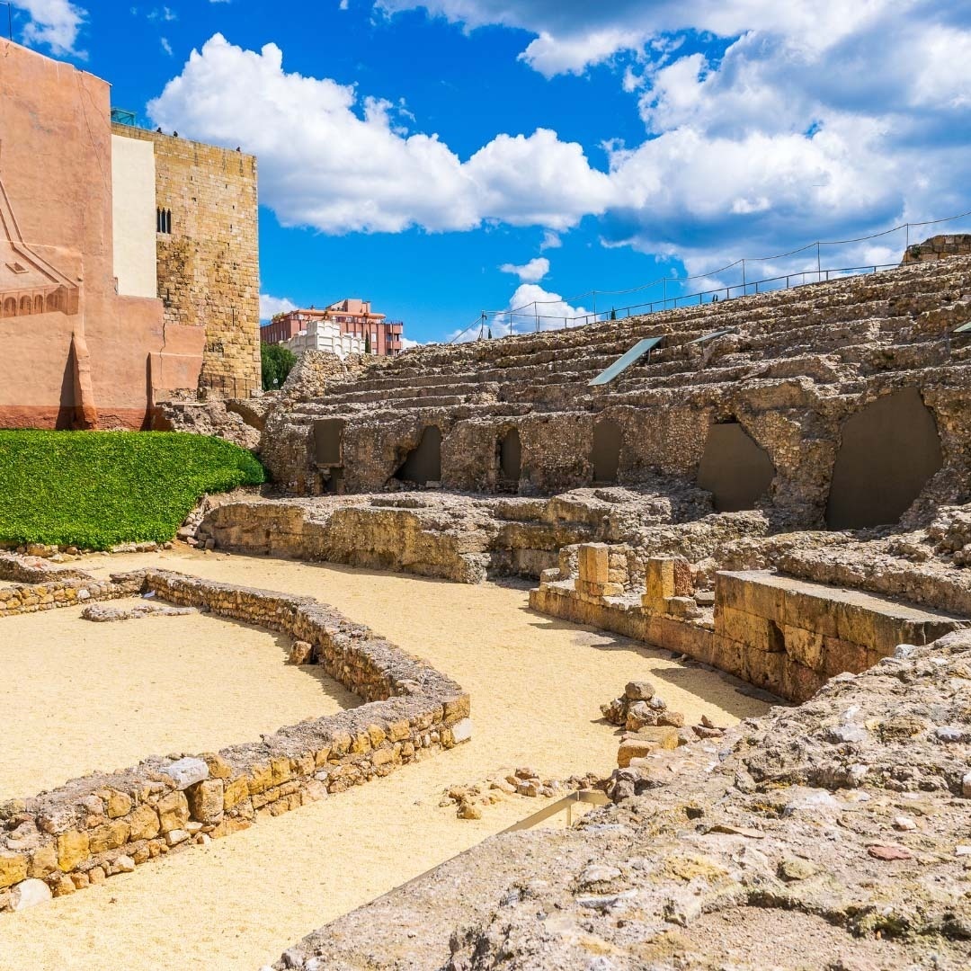 the ruins of an ancient amphitheater with a building in the background