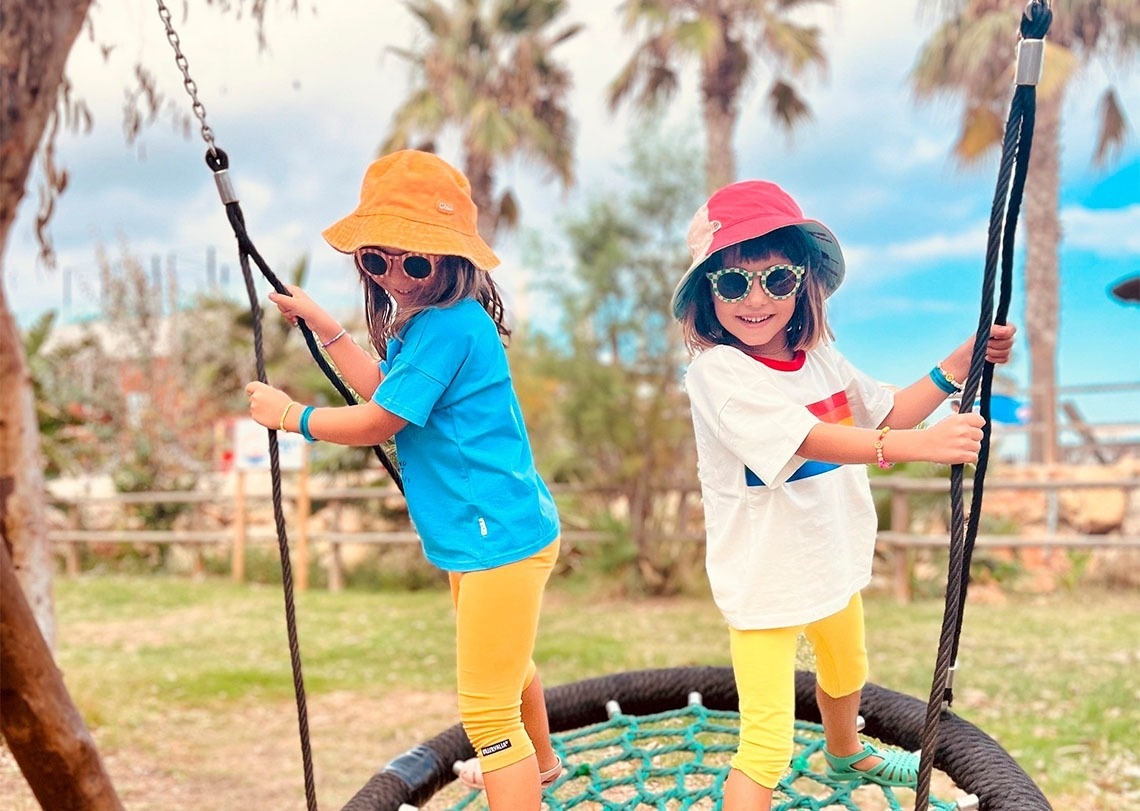 two little girls wearing hats and sunglasses are playing on a swing