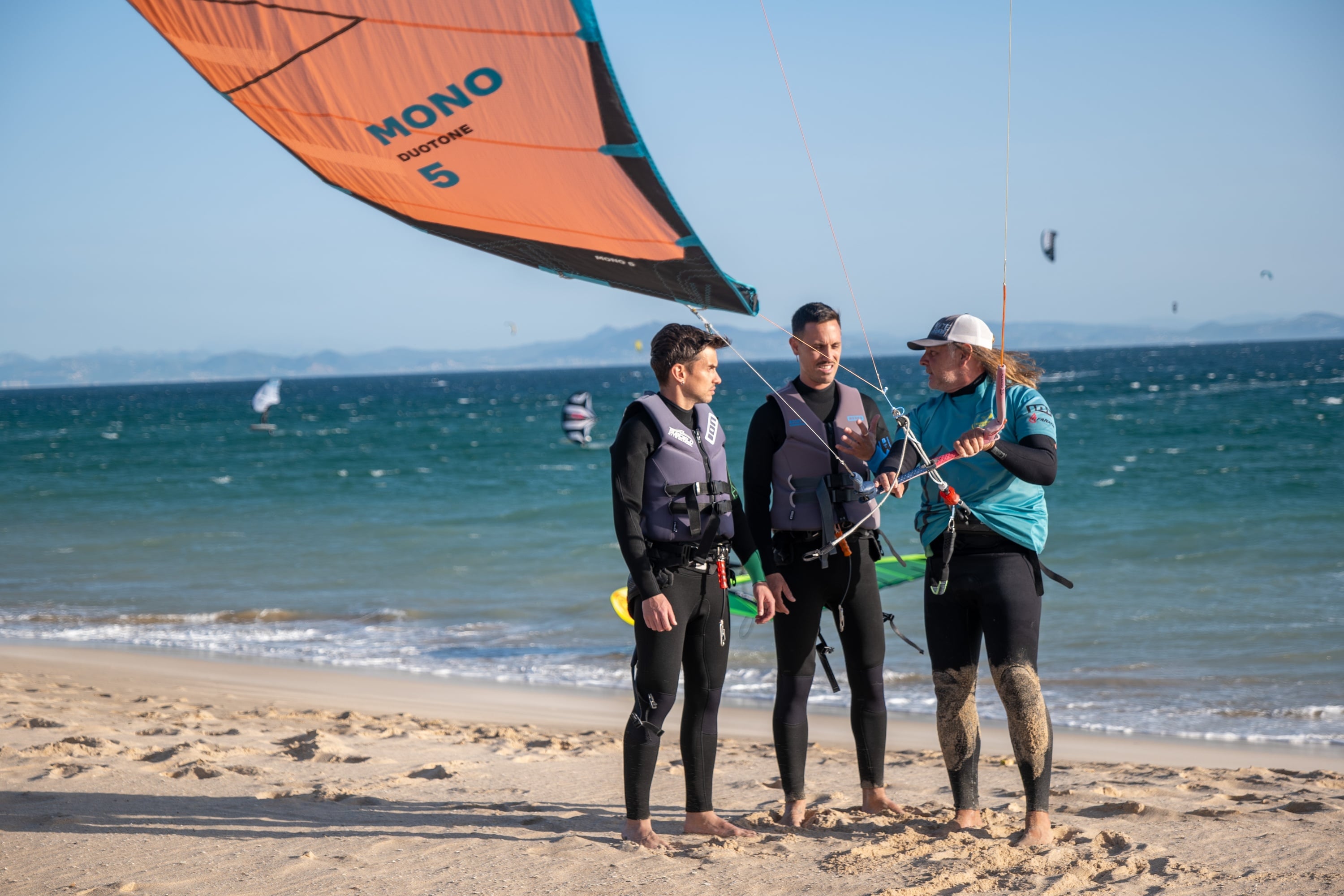Tres hombres hablando en la playa con un kite.
