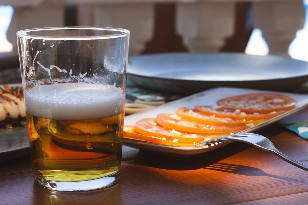 een glas bier naast een bord tomaten en een vork