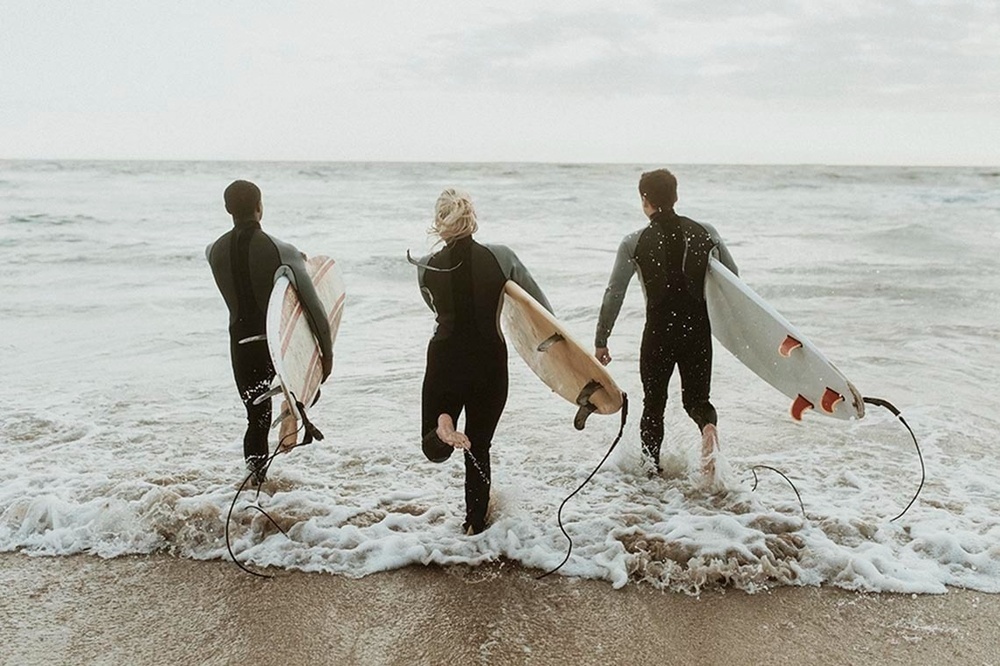 tres surfistes corren a través de l' aigua a la platja