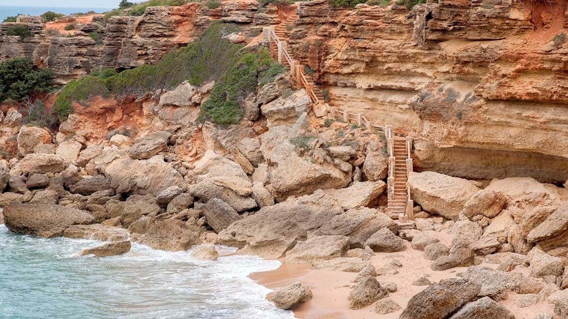 una escalera de madera conduce a una playa a lo largo de un acantilado rocoso