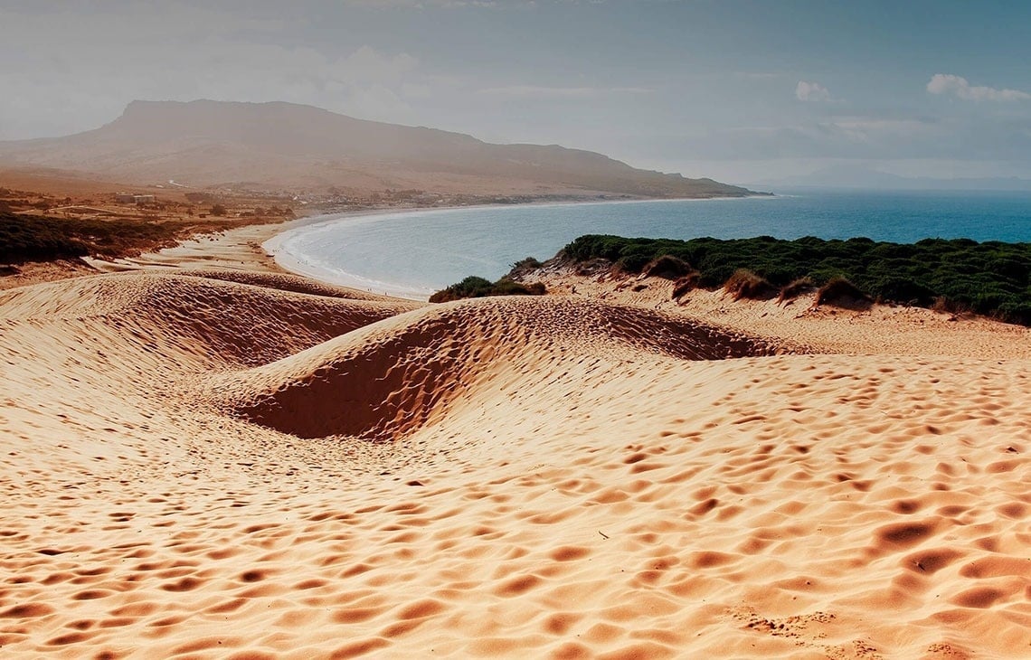ein sandiger Strand mit einem Holzzaun im Vordergrund