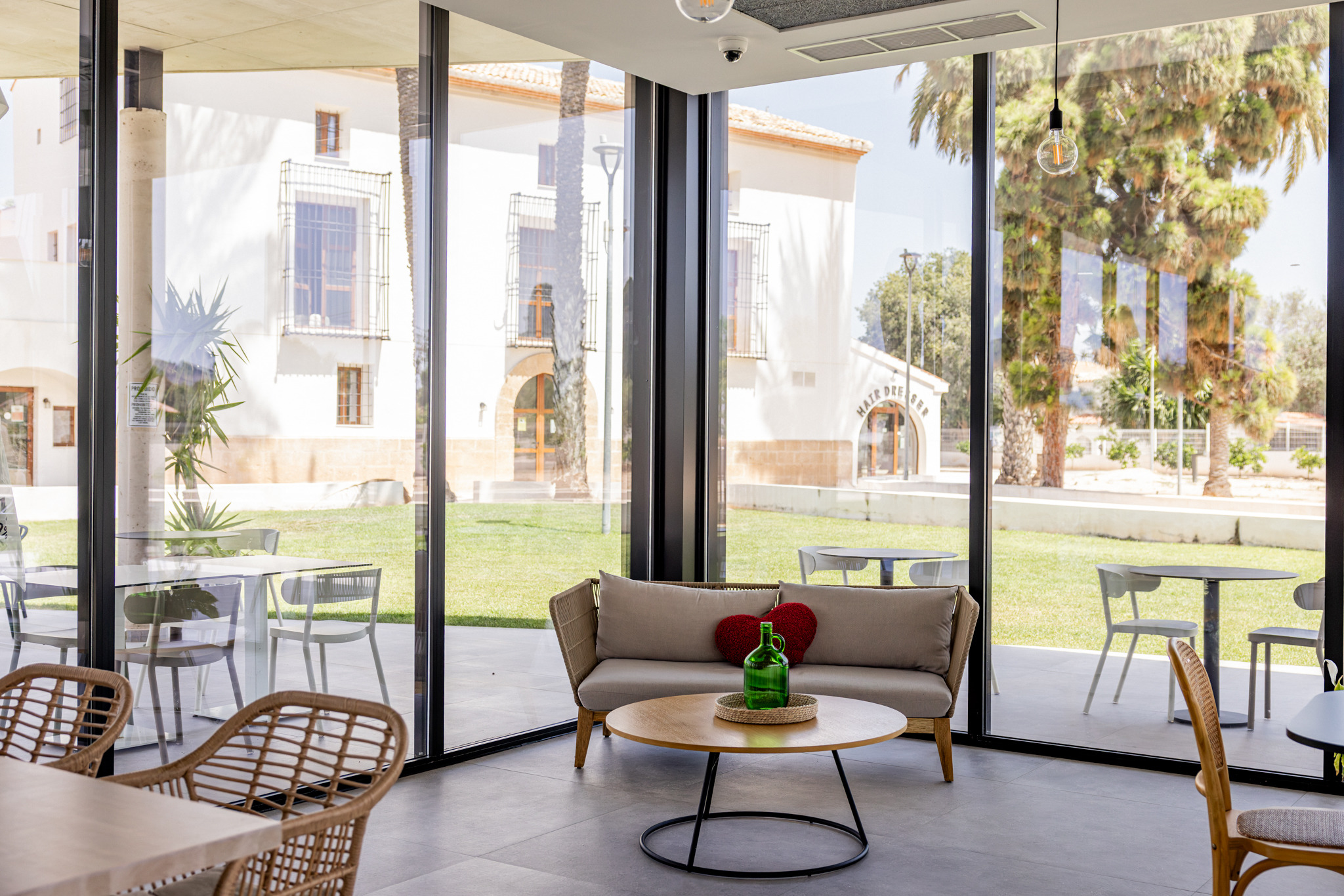 Taiga: Corporativa: moderno salón con sofá, mesa y vistas al exterior con palmeras.