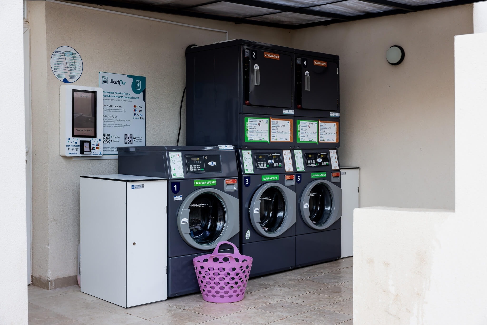 una mujer sostiene una canasta azul llena de ropa en una lavandería