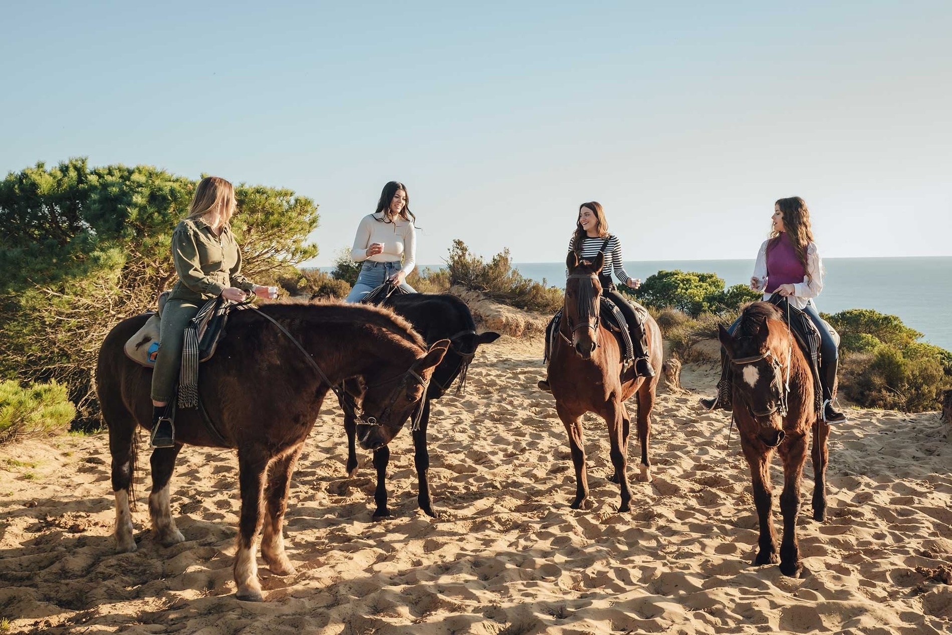 four women are riding horses in the sand near the ocean