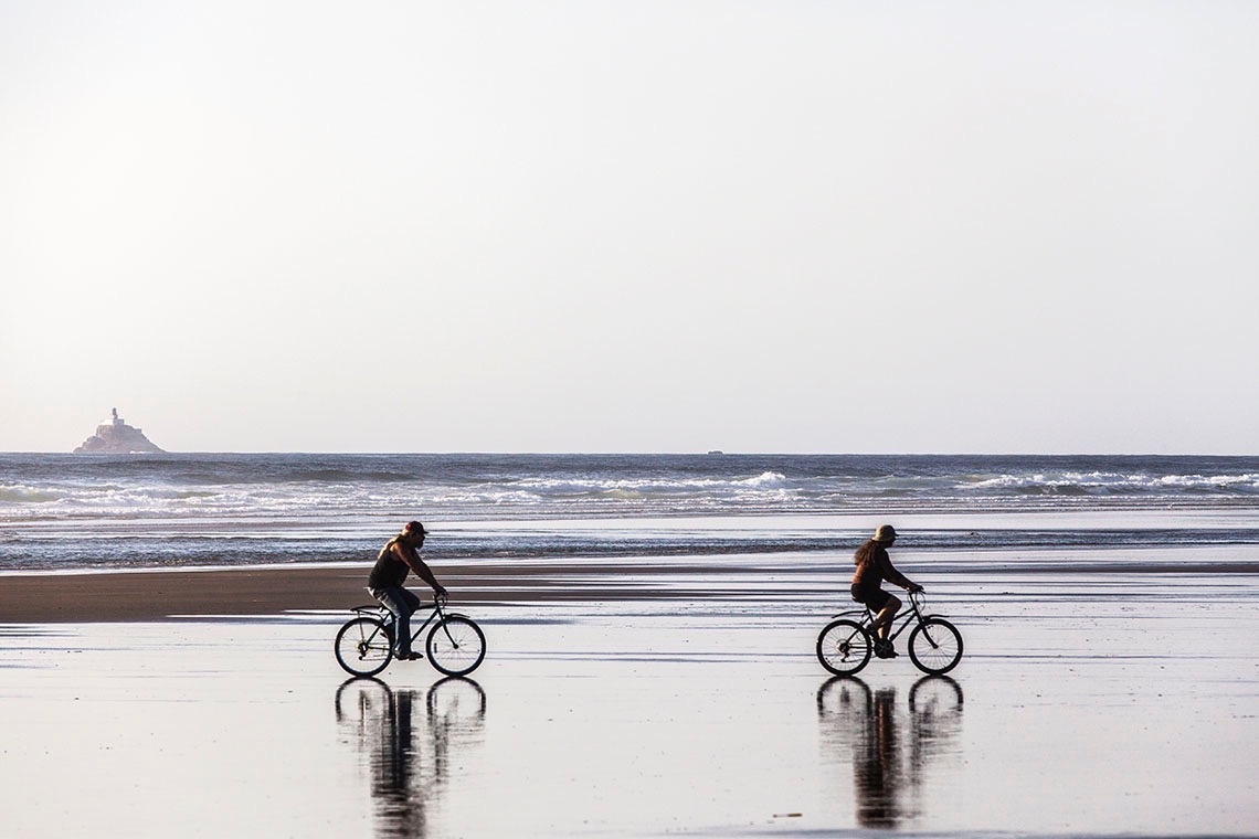 twee mensen fietsen op het strand met de oceaan op de achtergrond