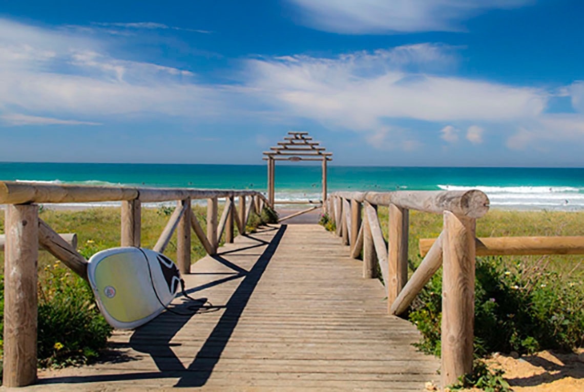 een surfplank ligt op een houten loopbrug naar de oceaan