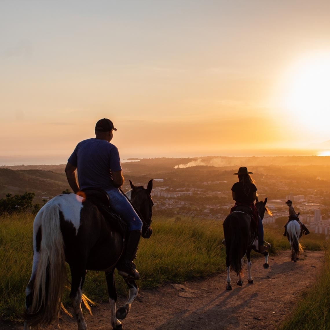 un hombre y una mujer montan a caballo por un camino al atardecer