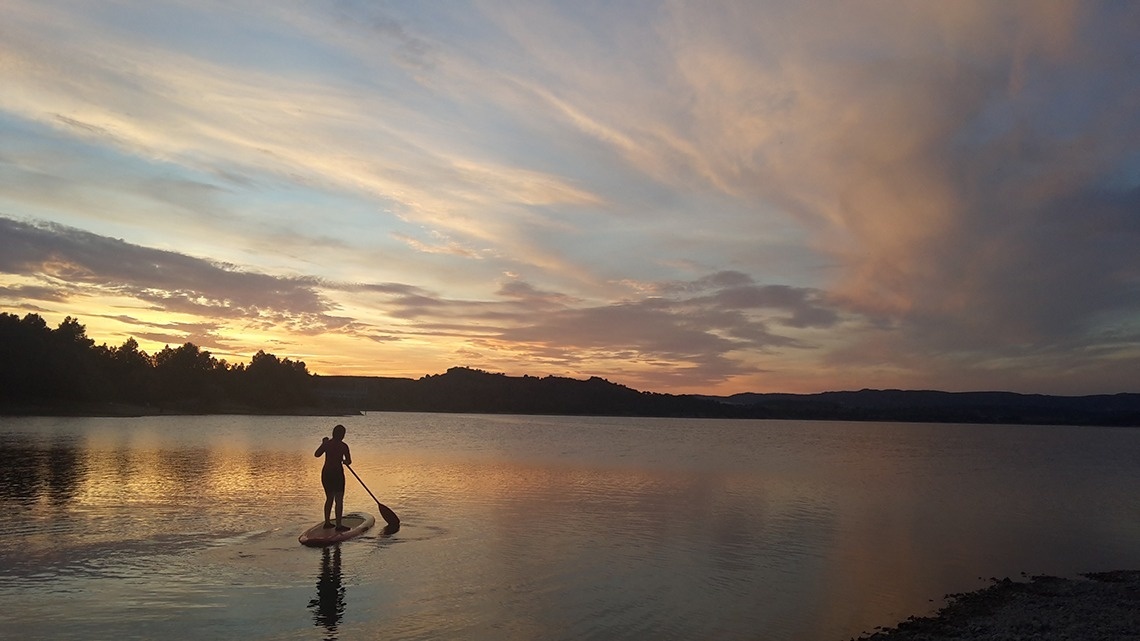 una persona navega en una paddle board a un llac al atardecer