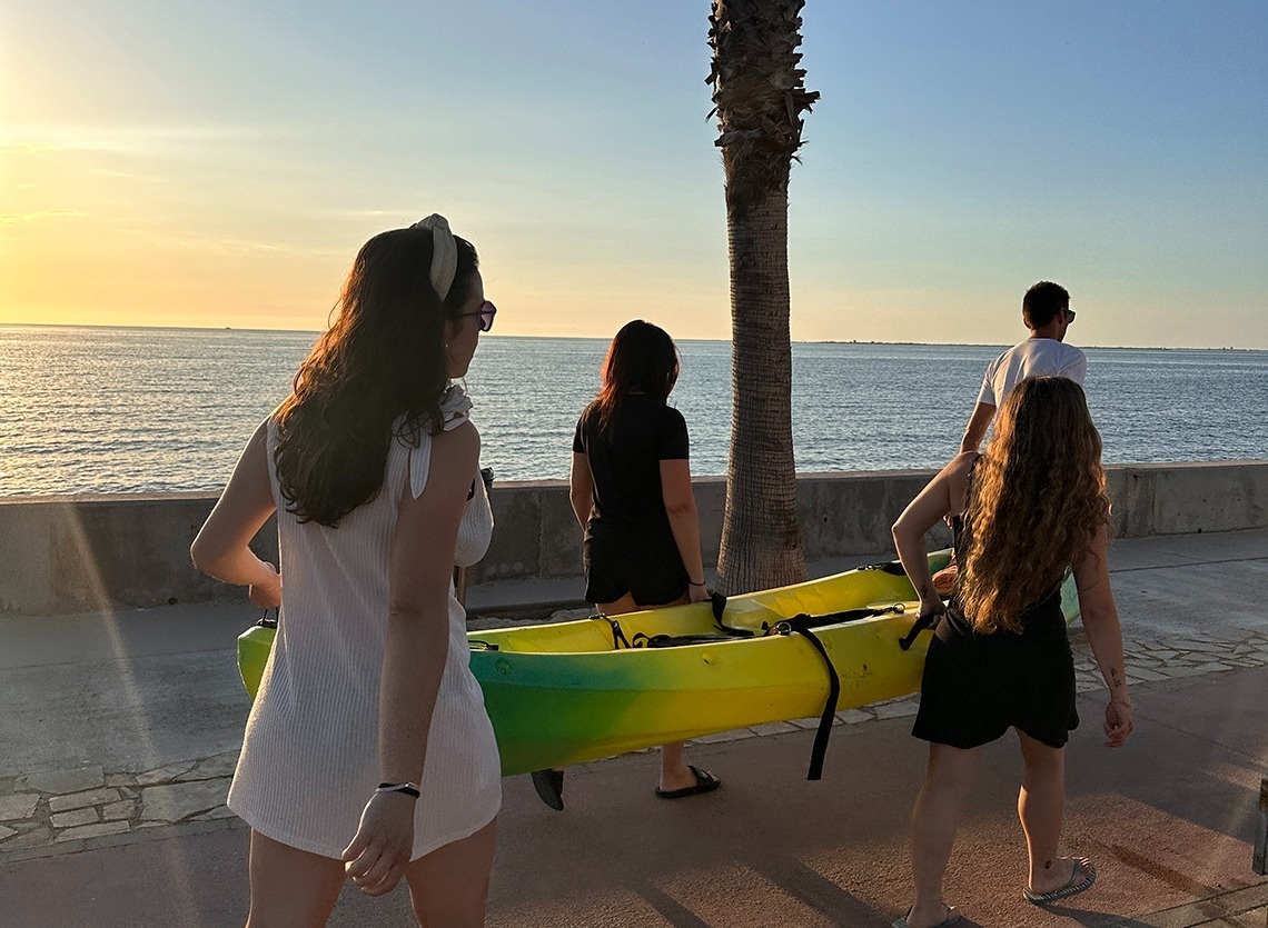 une femme porte un canoë jaune et vert sur le trottoir