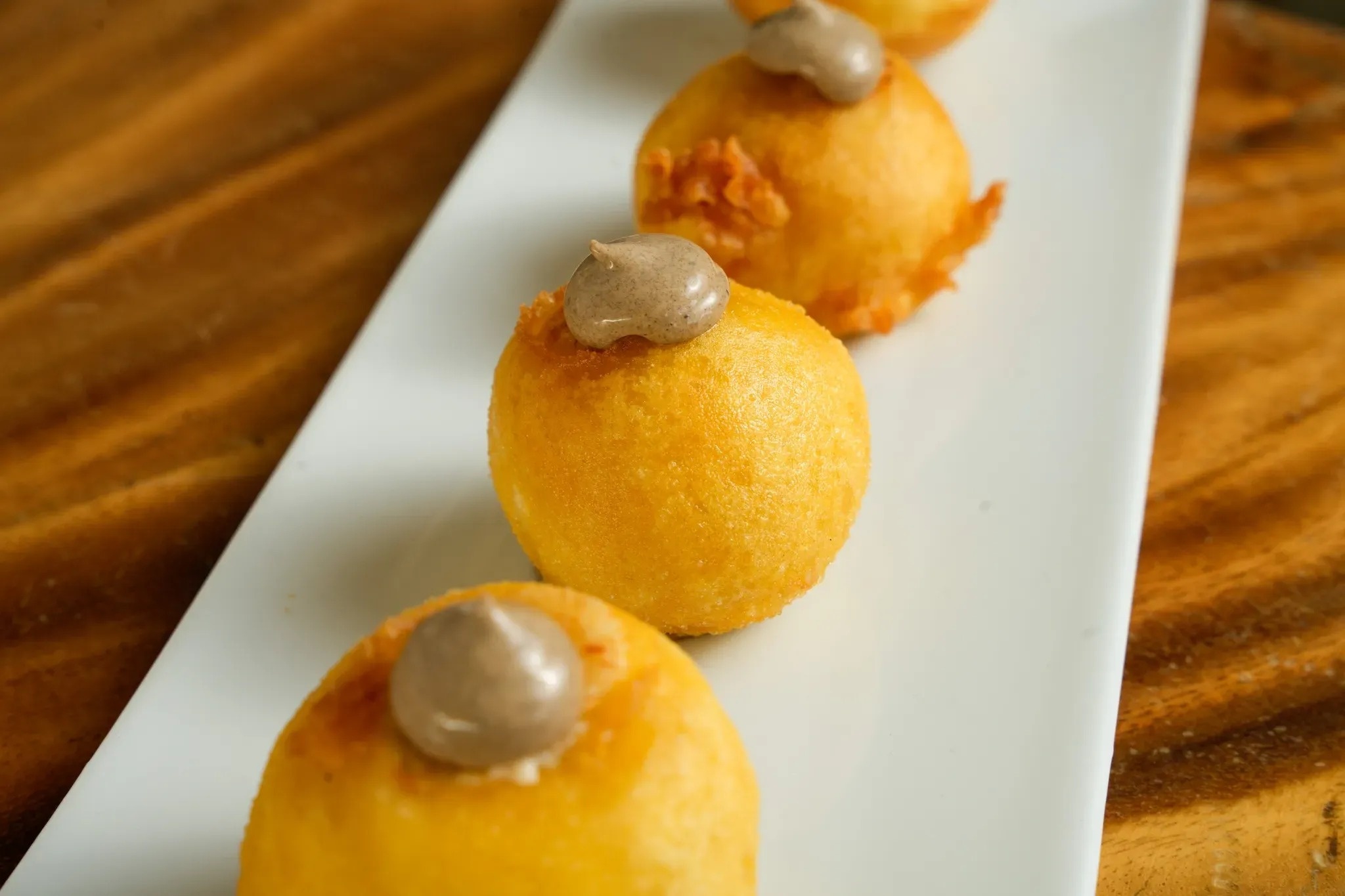 a white plate topped with three fried food balls with chocolate sauce on top