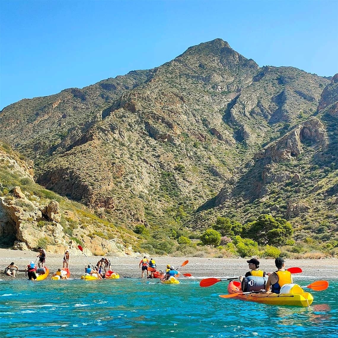 un grupo de personas en kayaks en el agua con montañas en el fondo