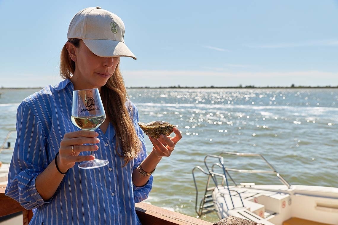 een vrouw houdt een glas wijn vast en eet een oester