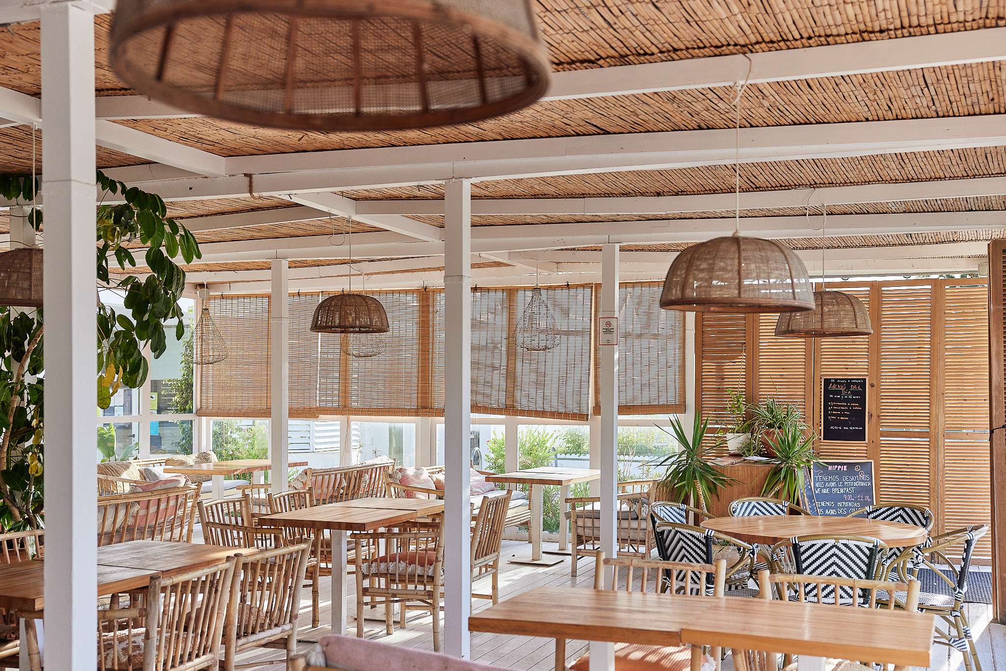Ambiente relajado en hotel con mesas de madera, sillas de mimbre y luces colgantes. Taiga: Corporativa