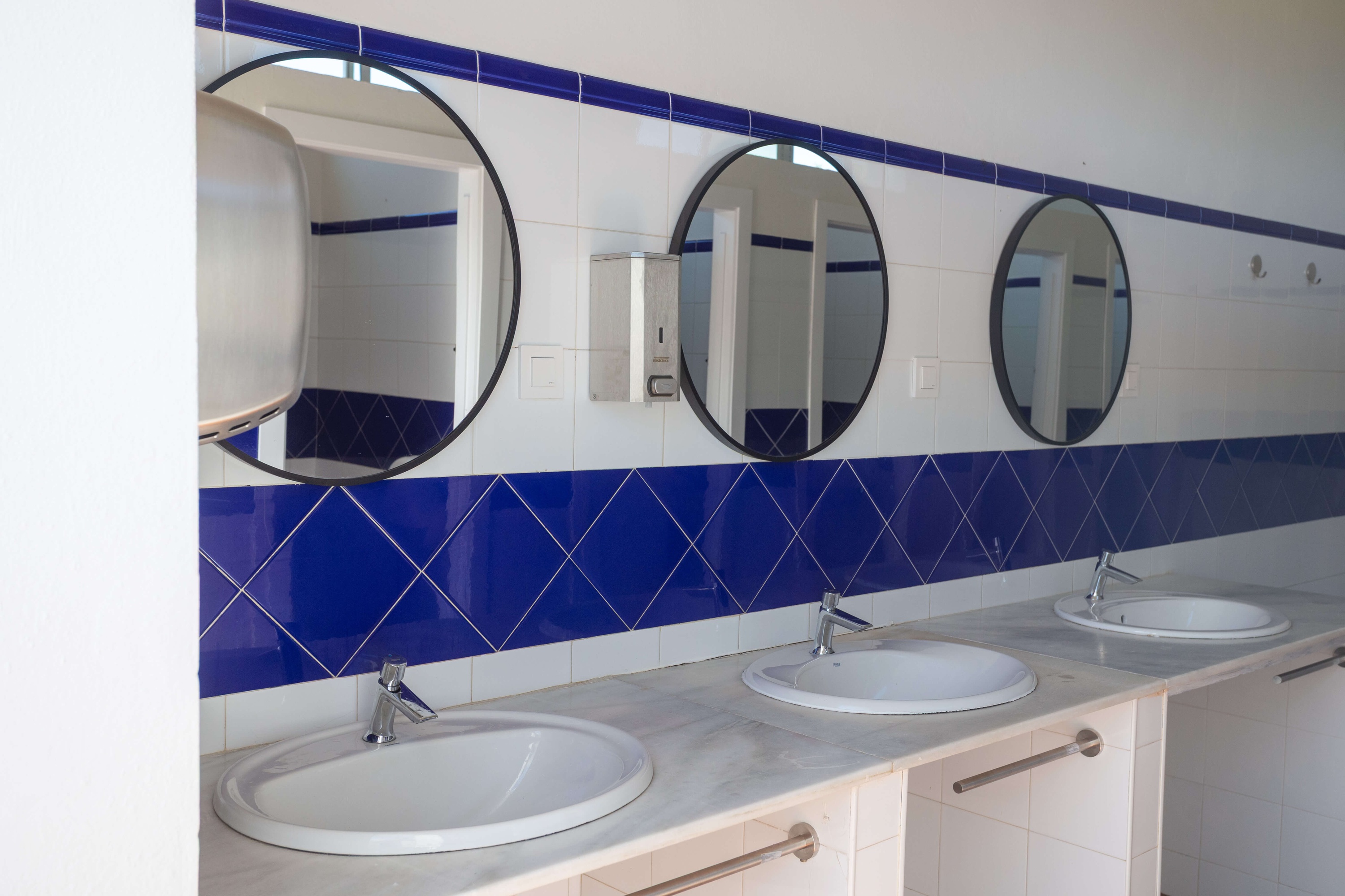 Lavabo d'hotel net i funcional amb rajoles blaves, miralls rodons i rentamans. Taiga: Corporativa.