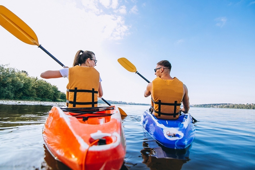 un home i una anciana remen en kayaks en un riu