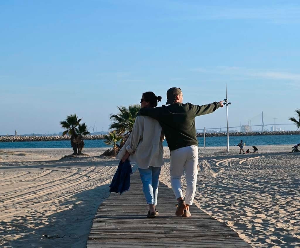 un homme et une femme marchent sur une jetée en bois vers l' océan