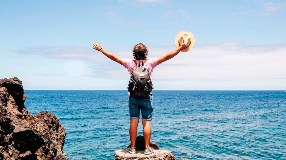 un hombre con una mochila y un sombrero se para en un acantilado mirando al océano