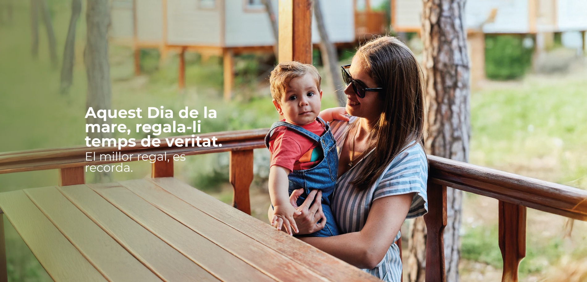 Una familia feliz disfruta de un momento de interacción y alegría con su hijo pequeño en la terraza de una cabaña de madera, rodeada de un entorno natural y boscoso.