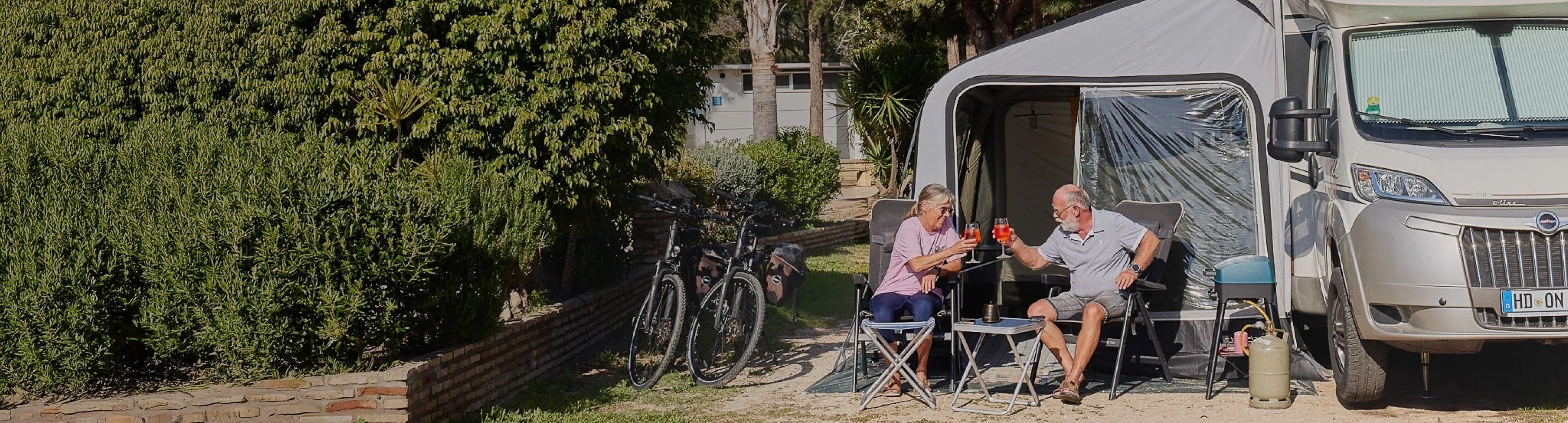 a man and a woman sit in chairs in front of a camper van that says descansa sin prisas