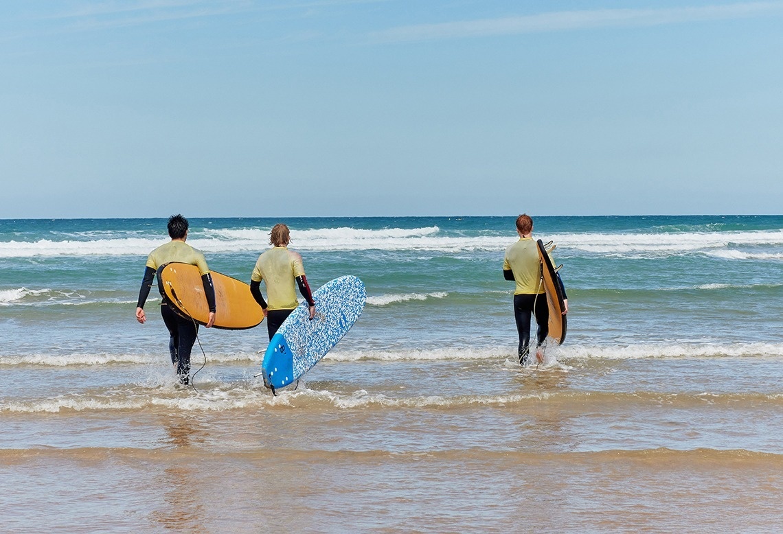 tres surfistas caminan por la playa con sus tablas de surf