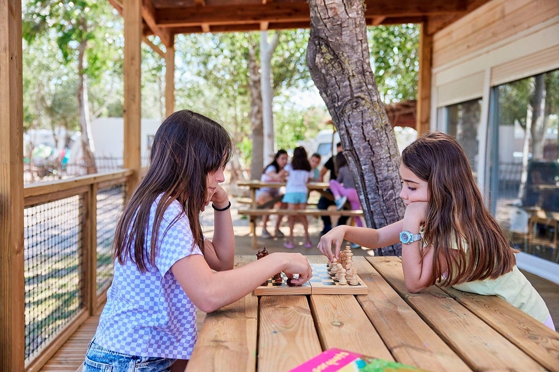 two girls are playing a game of chess on a wooden table