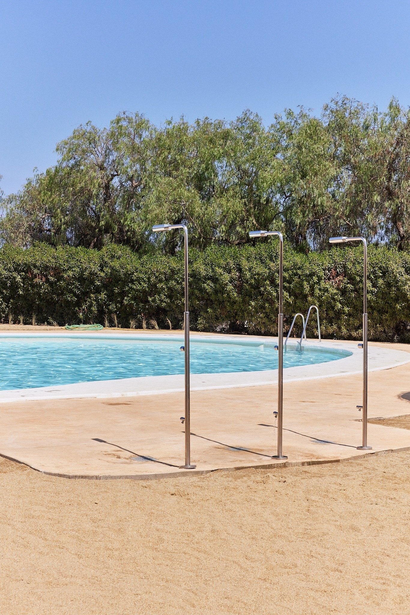 tres duchas de acero inoxidable están al lado de una piscina