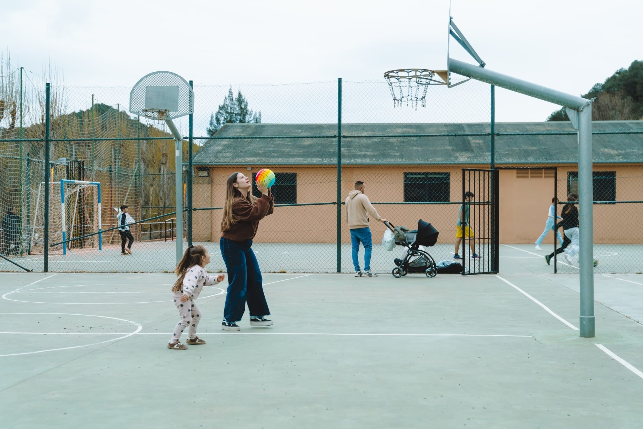 Familia disfrutando actividades al aire libre en cancha multideporte con niños y bebé.