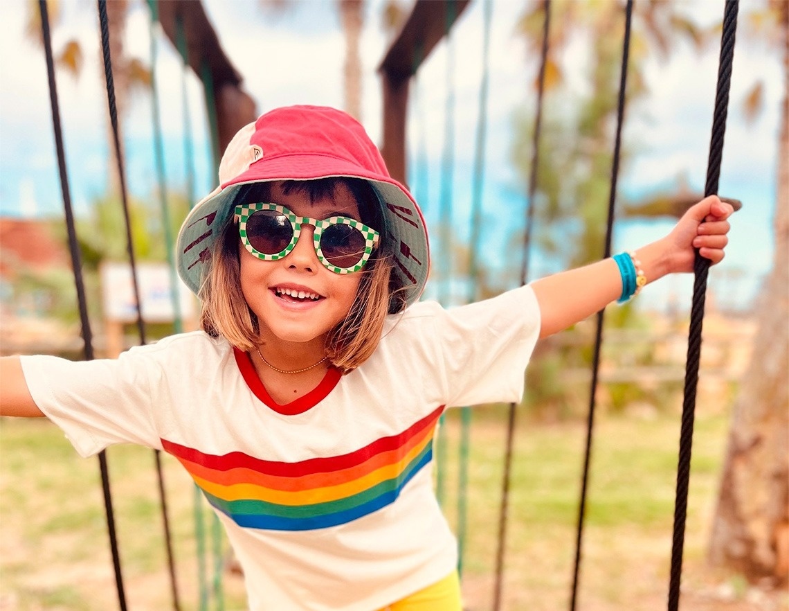 a little girl wearing sunglasses and a hat is playing on a swing