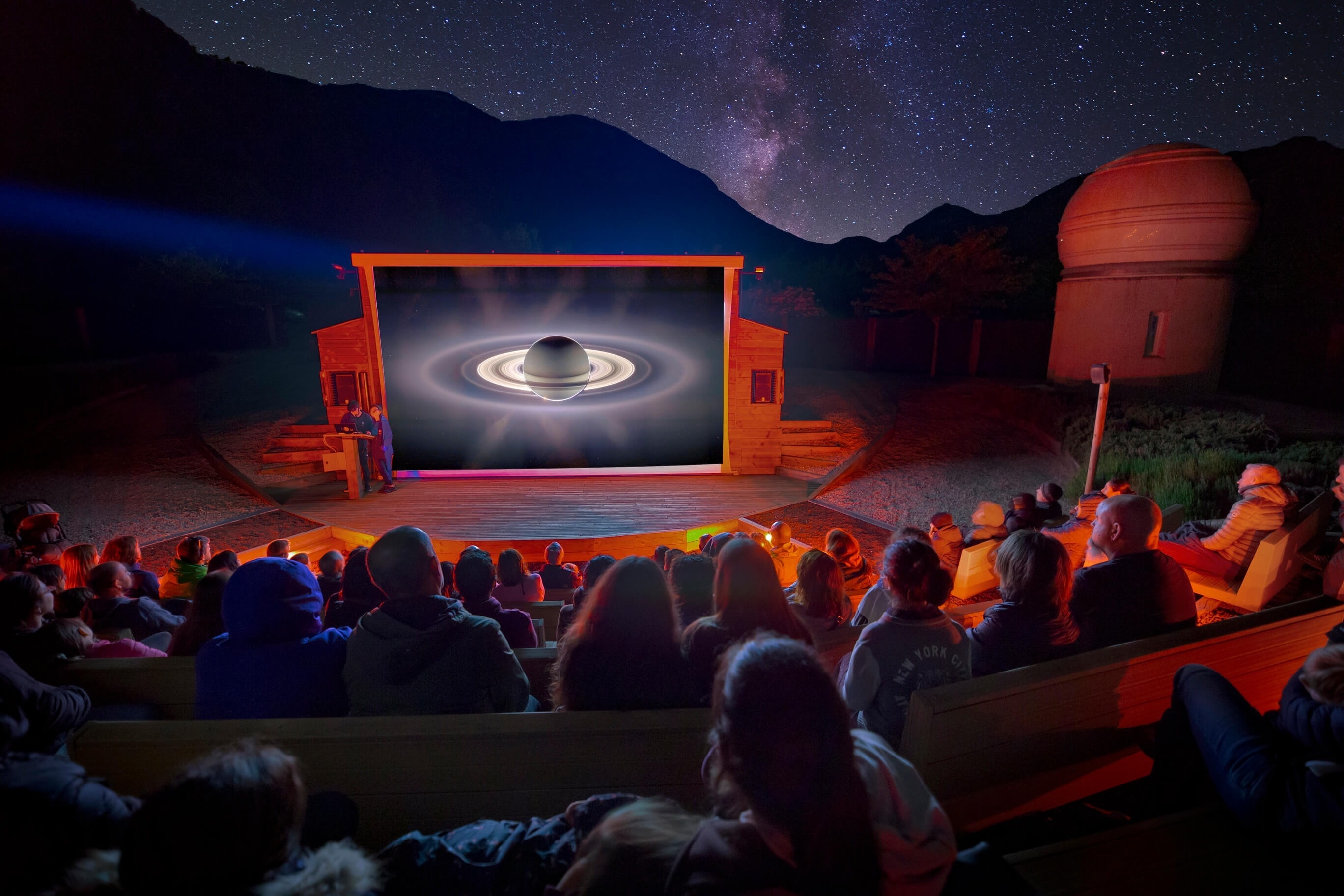 Huéspedes disfrutan show astronómico al aire libre con proyección de Saturno bajo cielo estrellado y observatorio.