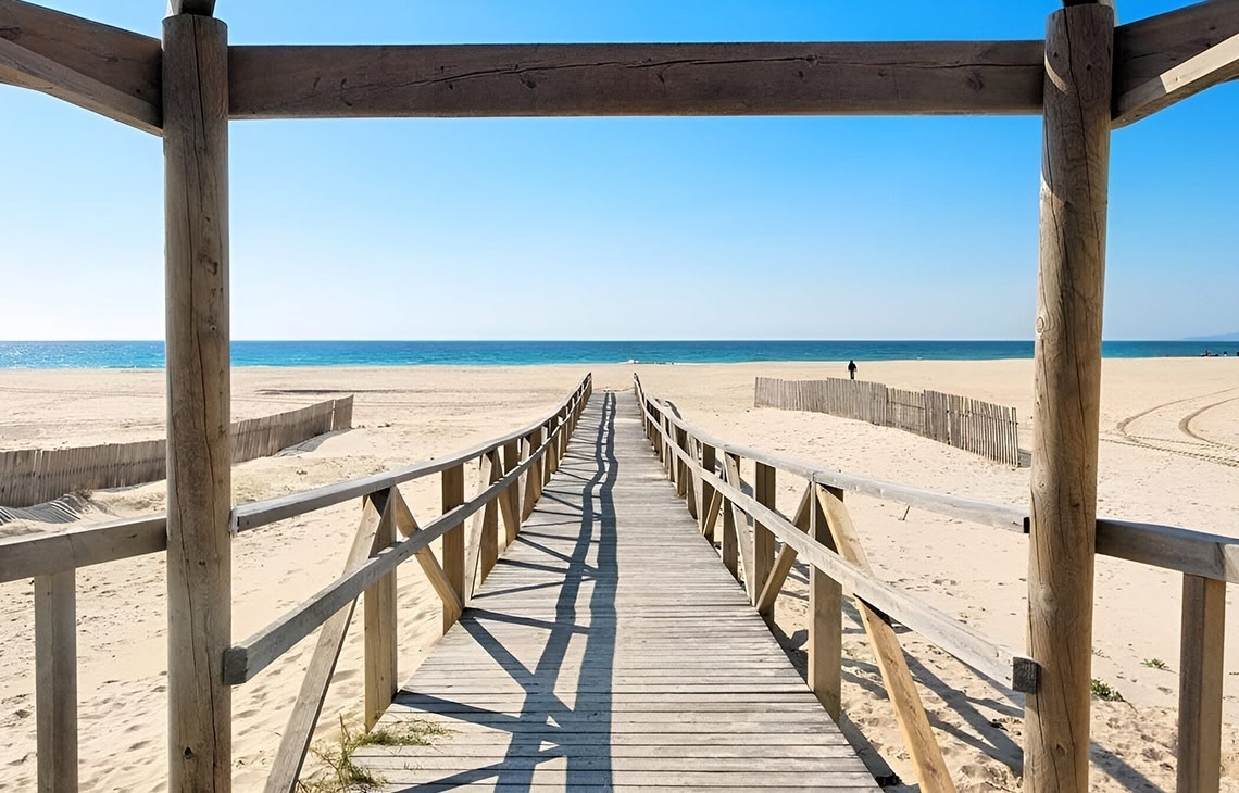 ein sandiger Strand mit einem Holzzaun im Vordergrund
