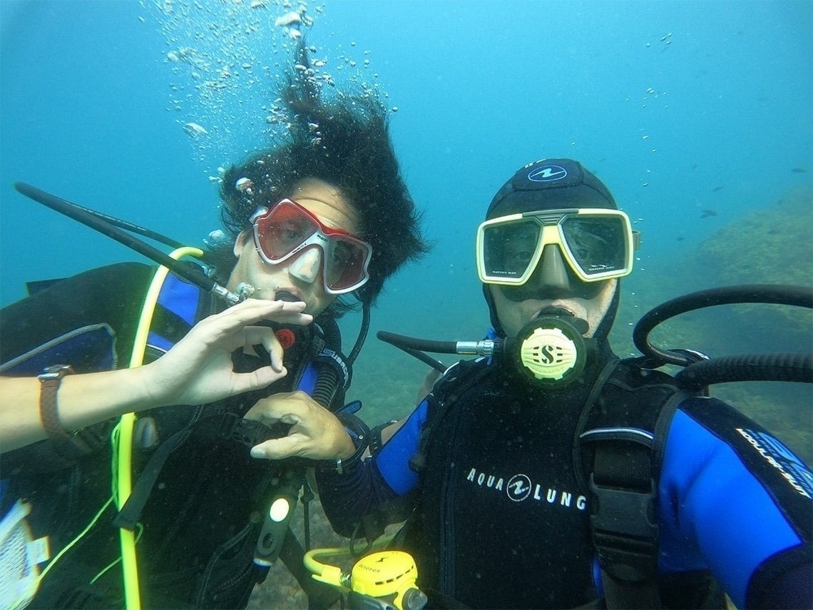 two scuba divers are posing for a picture and one is wearing an aqualung shirt