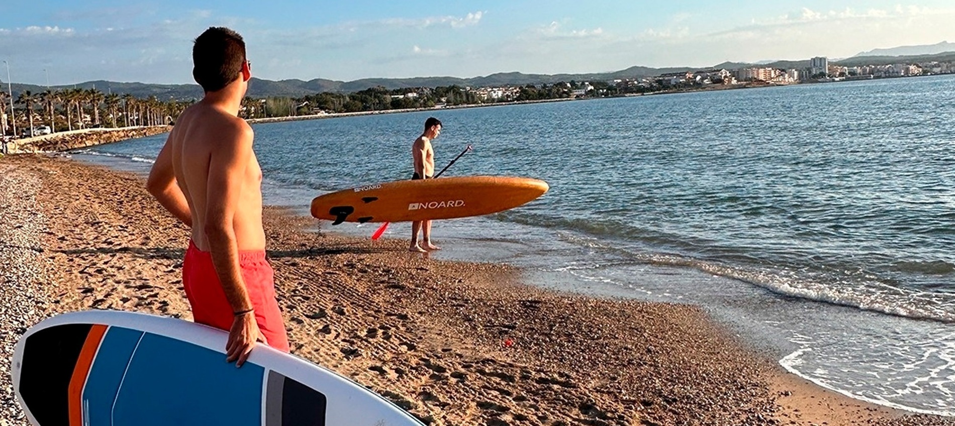 two men standing on a beach holding surfboards one of which has the word india on it