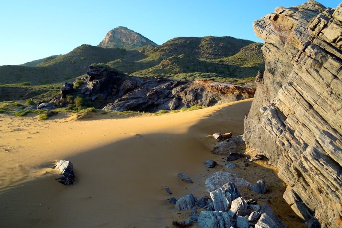 ein sandiger Strand mit einem großen Felsen im Vordergrund