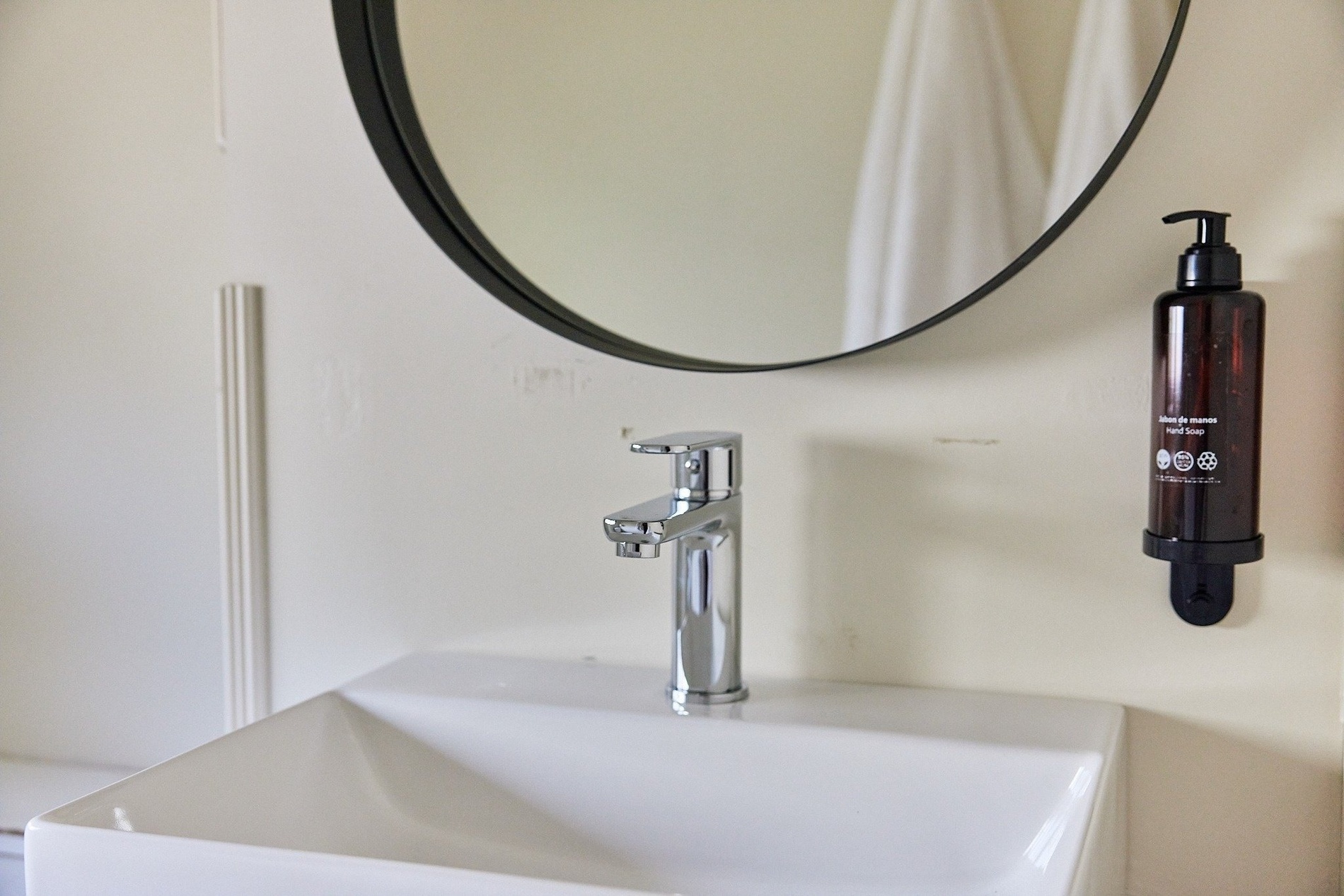 a bathroom sink with a round mirror and a bottle of hand soap