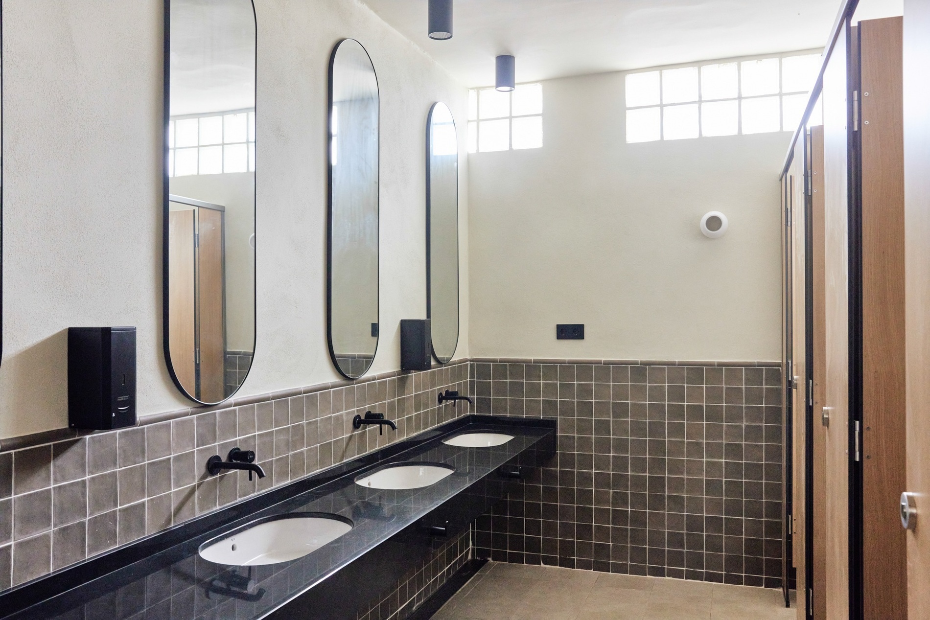 un baño con tres lavabos y un dispensador de jabón