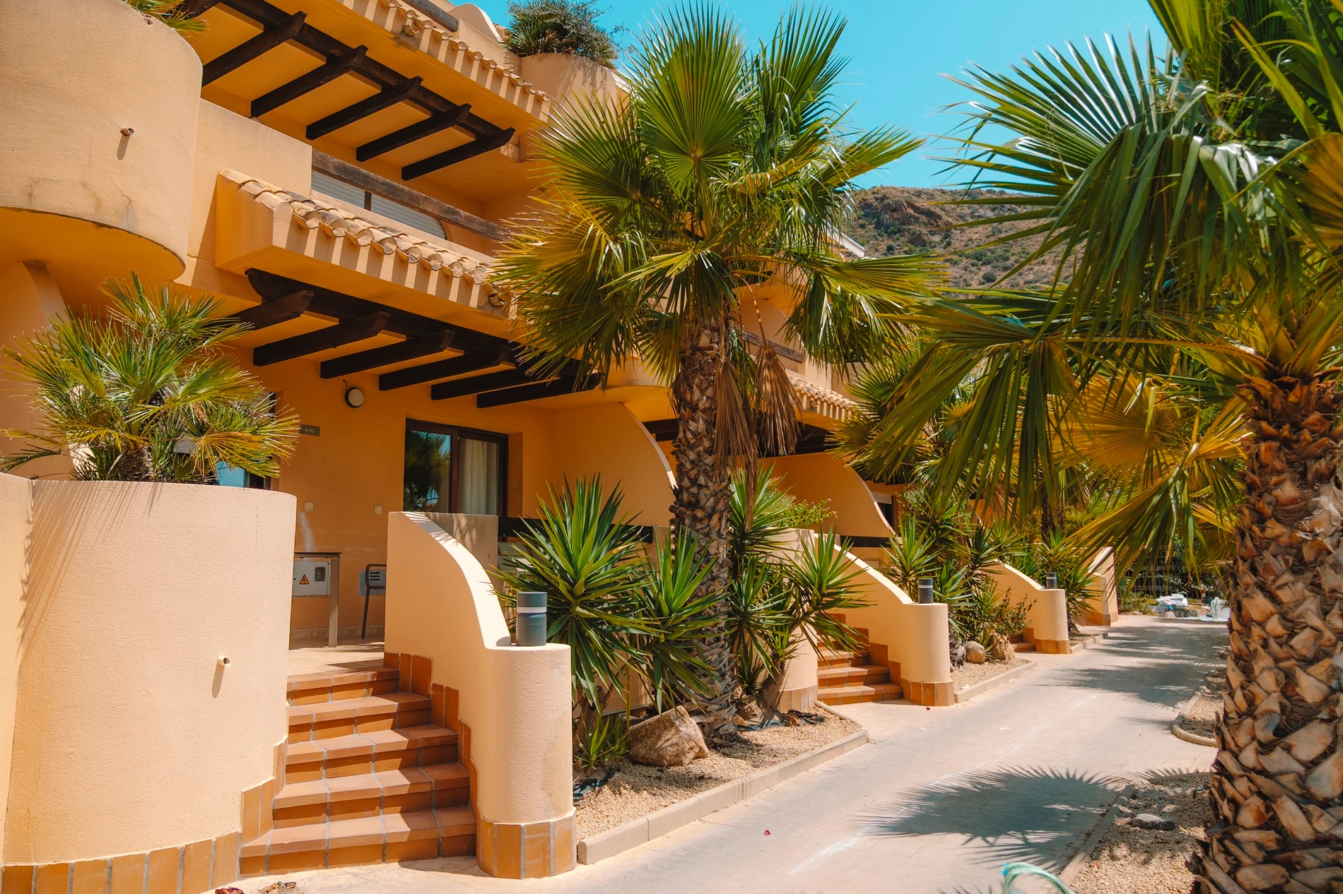 Edificio de hotel tropical con palmeras y entrada: TAIGA Costa Calida vacacional en España.