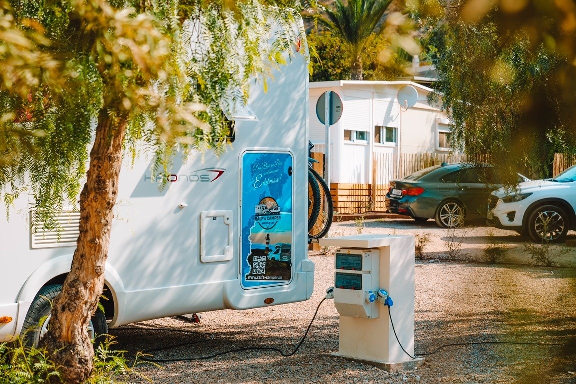 un rv blanco está estacionado junto a un árbol