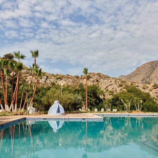 a large swimming pool with palm trees and mountains in the background