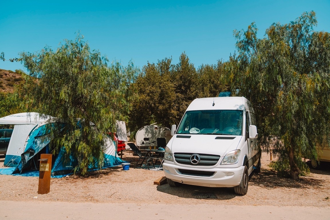 una furgoneta blanca está estacionada en un camping rodeado de árboles
