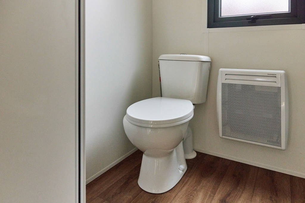 un inodoro blanco está junto a un radiador y una ventana