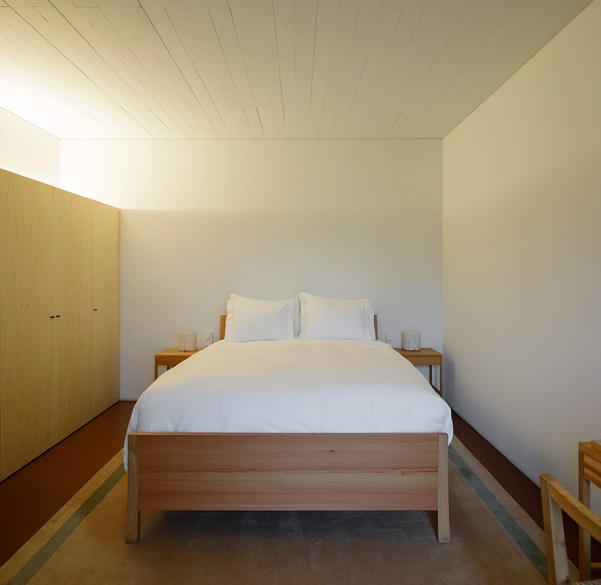 Dormitorio minimalista en Quinta do Outeiro con cama doble y armario de madera.