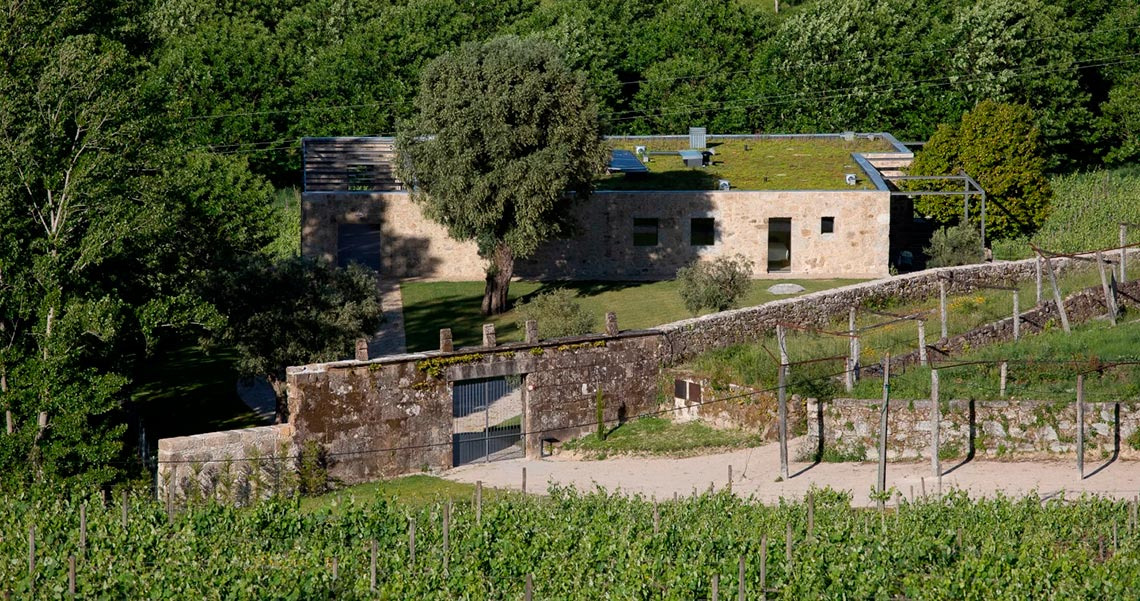 Casa rural en Quinta do Outeiro con tejado verde y muro de piedra.
