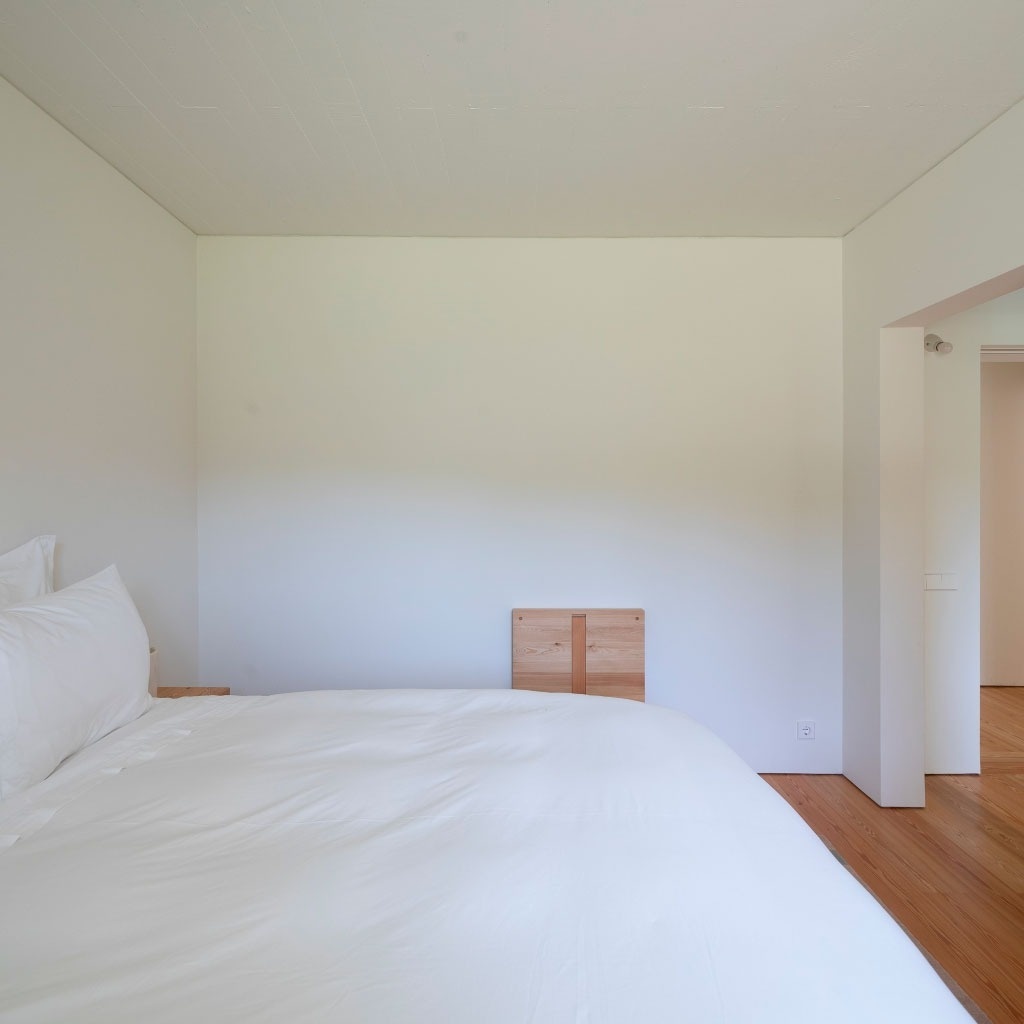 um quarto com uma cama branca e uma parede branca