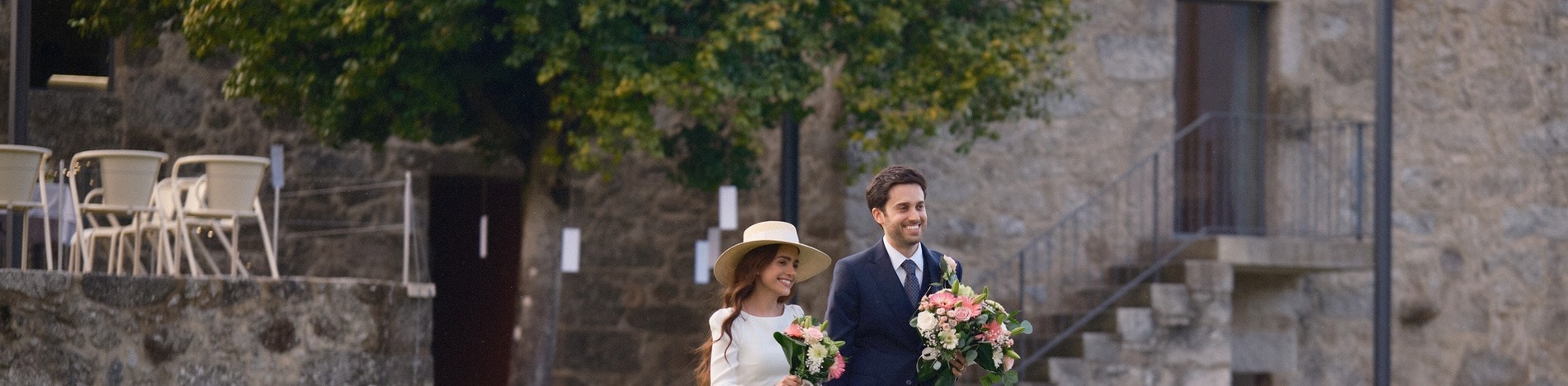 uma noiva e um noivo caminham em frente a um prédio de pedra