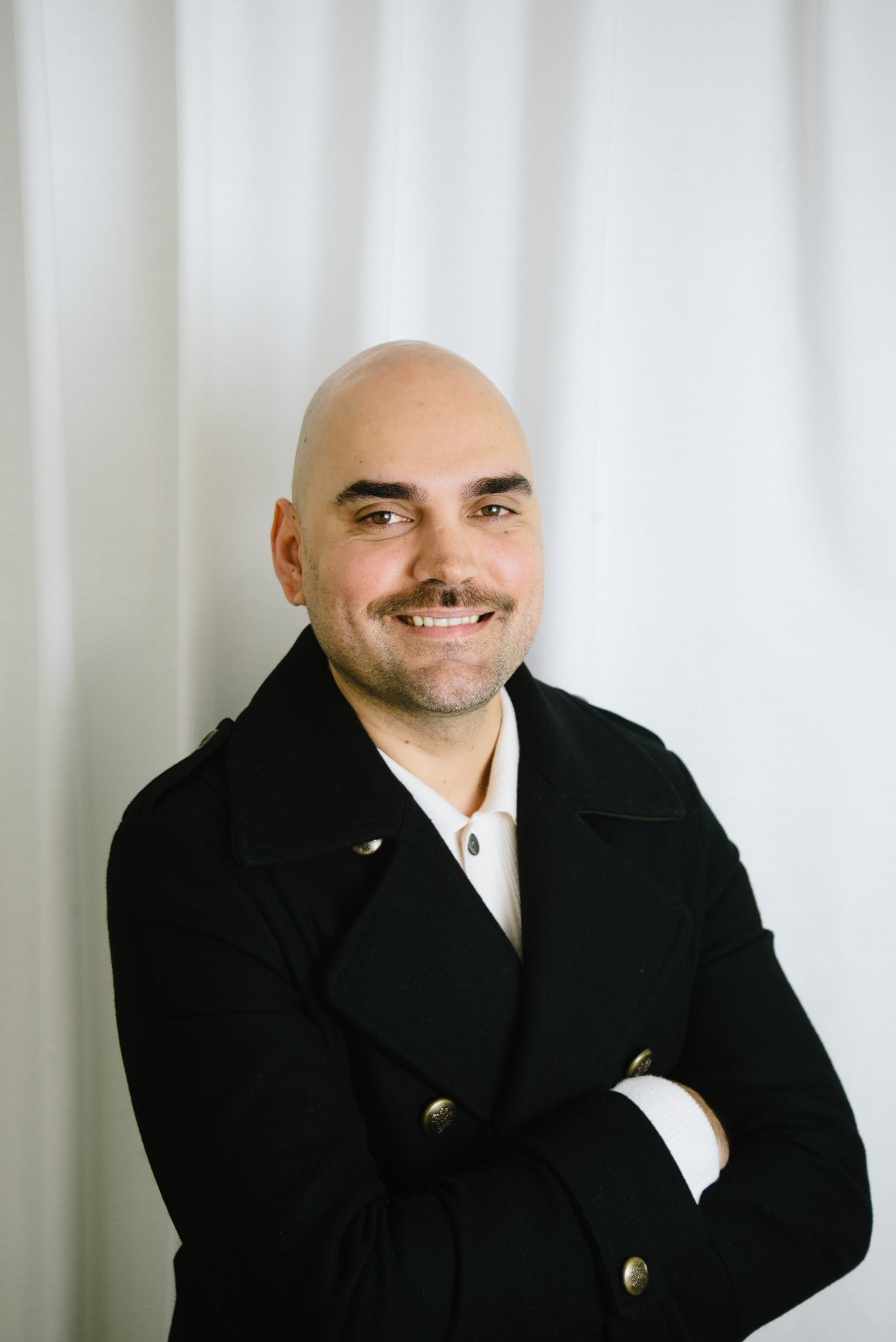 a bald man with a mustache is wearing a black coat