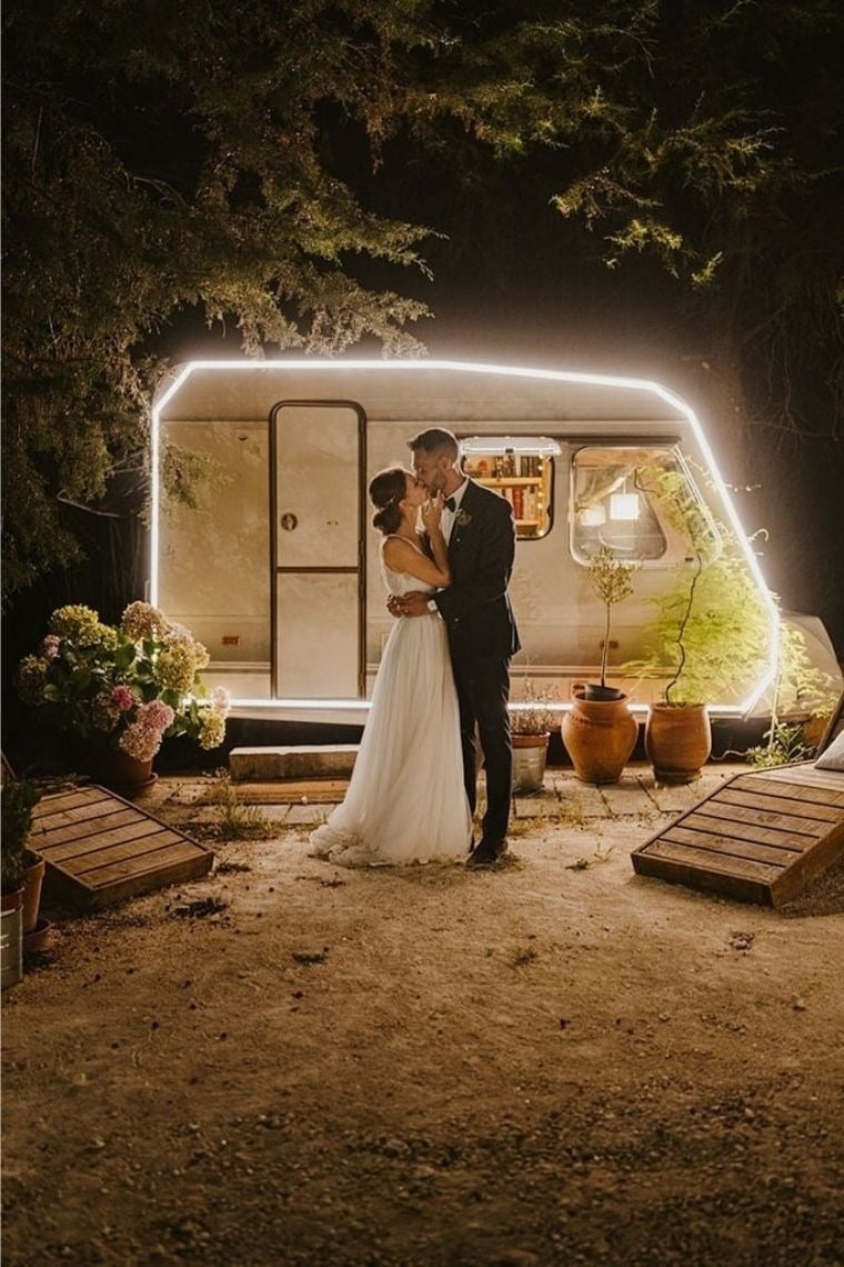 a bride and groom kiss in front of a camper