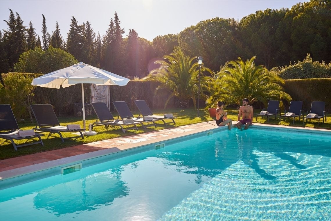 a man and woman sit on the edge of a swimming pool