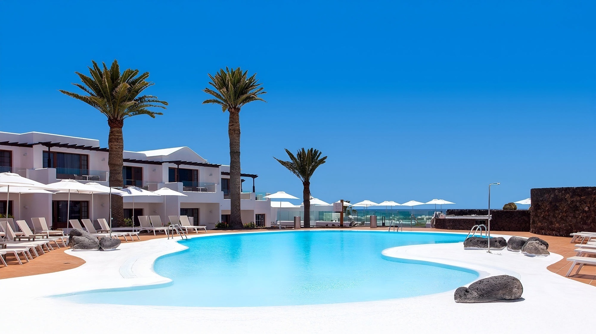 a large swimming pool surrounded by white chairs and umbrellas